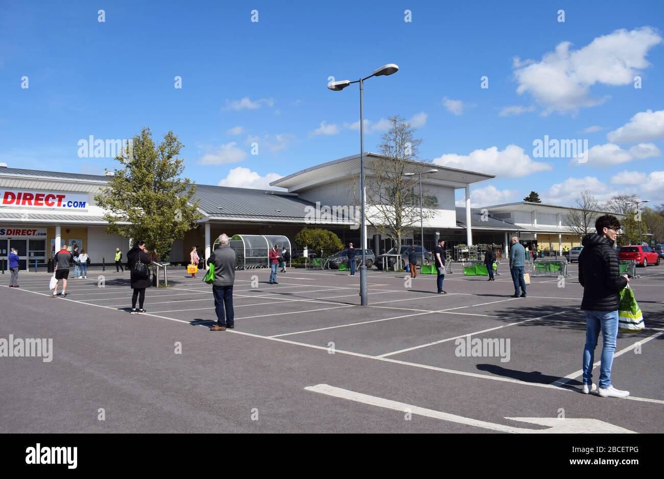 People queuing 2 meters apart in a car park while waiting to enter a supermarket to buy groceries in the UK during the Coronavirus Covid19 pandemic Stock Photo