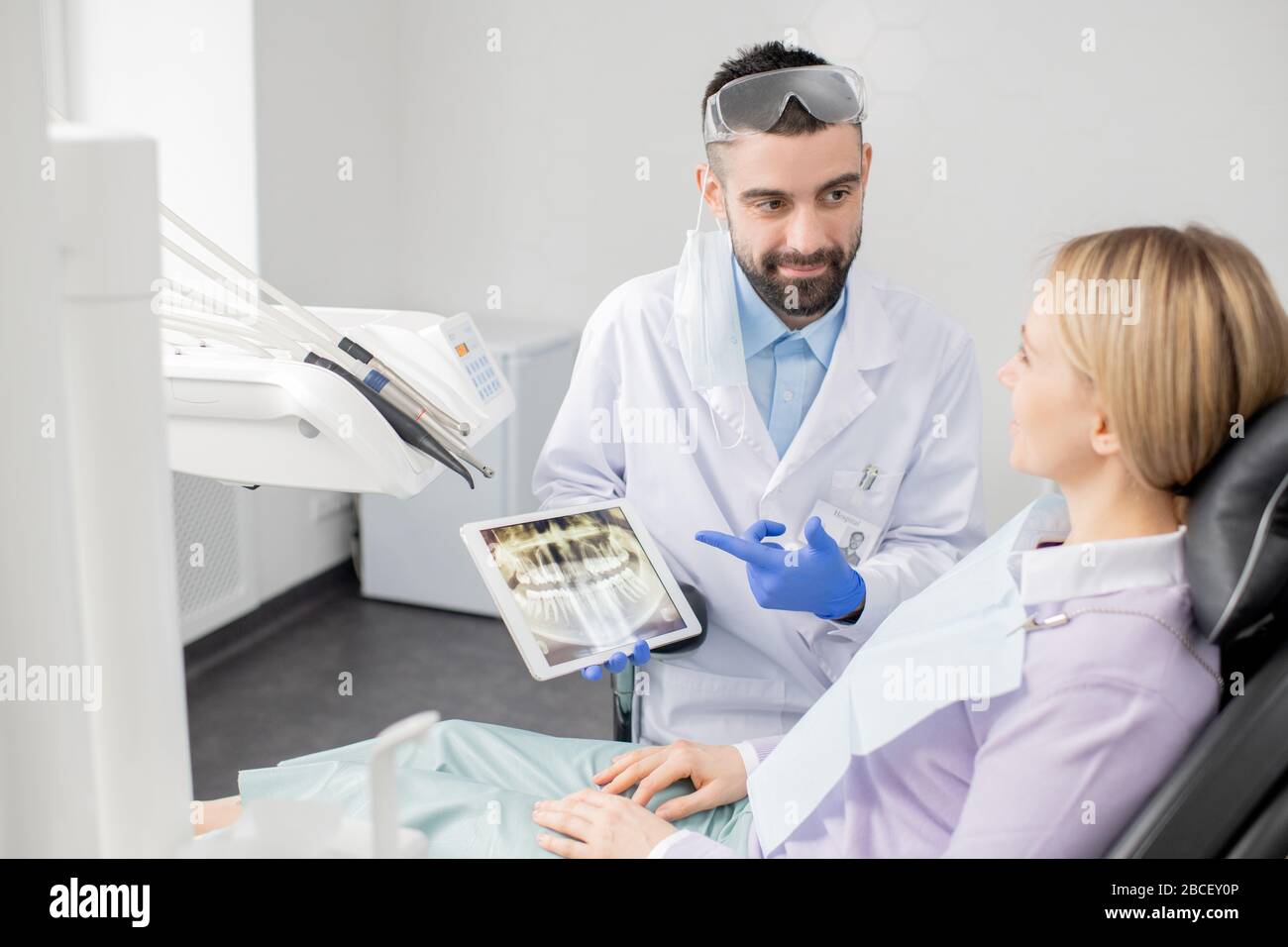 Young successful dentist in uniform pointing at touchscreen with teeth