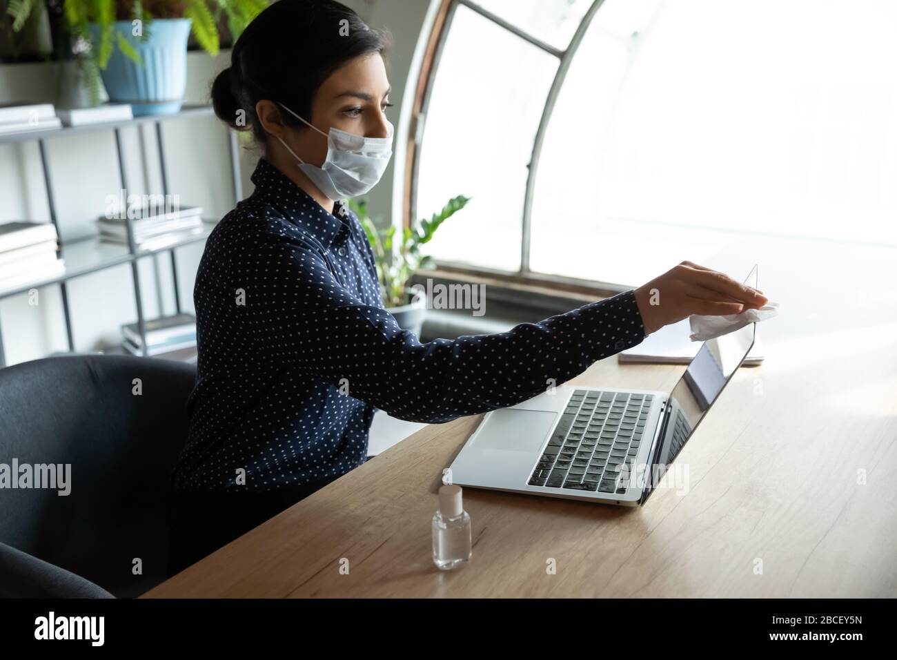 Young indian businesswoman using antiseptic sanitizer at workplace. Stock Photo