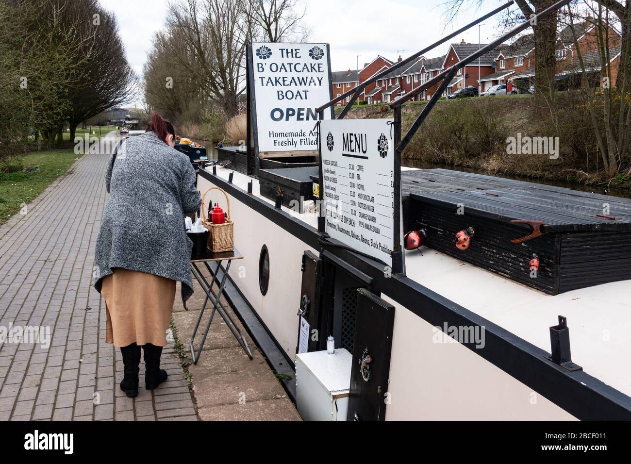 A woman buying food (Staffordshire oatcakes) from a narrowboat ()Que Sara Sara, the B'oatcake boat) on a canal, Stoke-on-Trent, Staffordshire, UK Stock Photo
