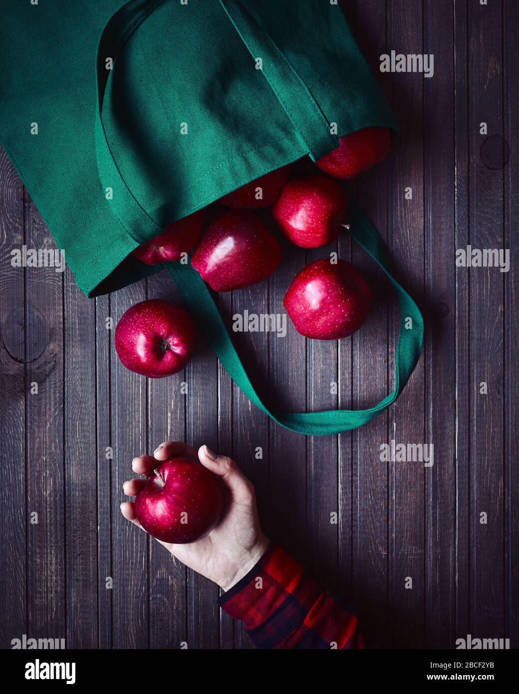 Online shopping delivery. Eco friendly bag with red apples. Woman holding apple on dark wooden background Stock Photo