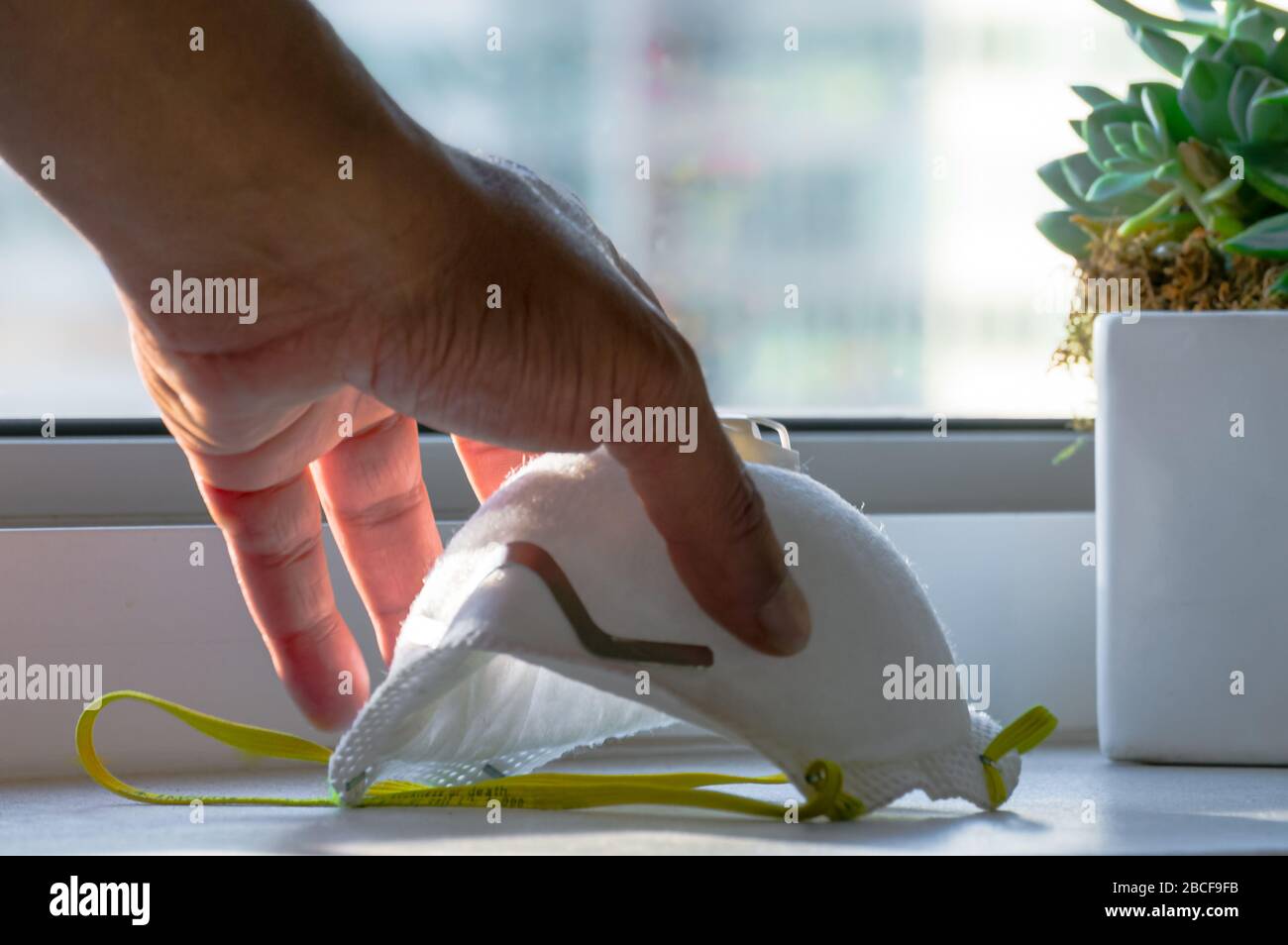 A male hand is picking up an N95 Face mask on a counter. Stock Photo