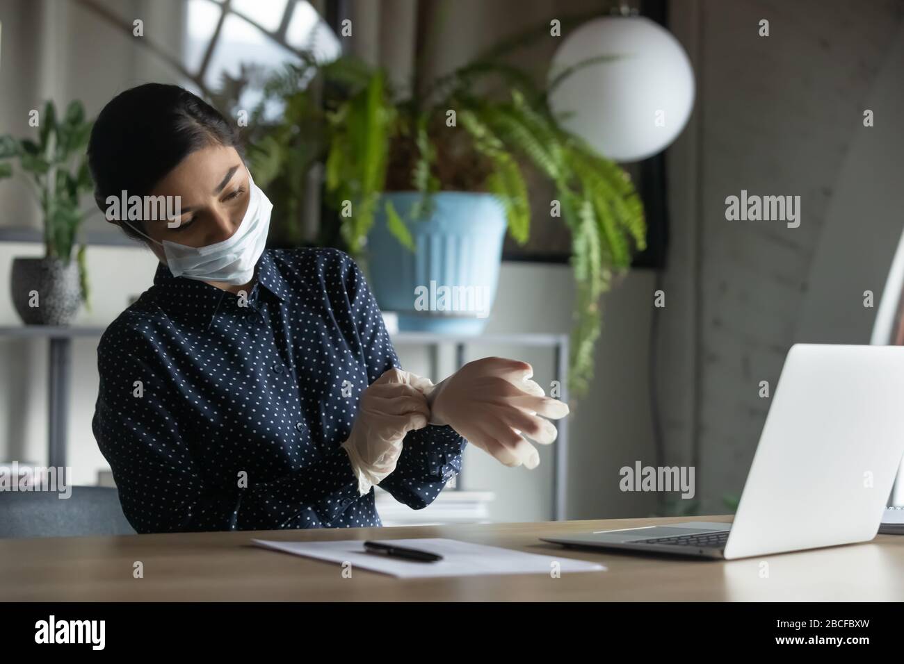 Young female company employee putting on medical gloves, starting workday. Stock Photo