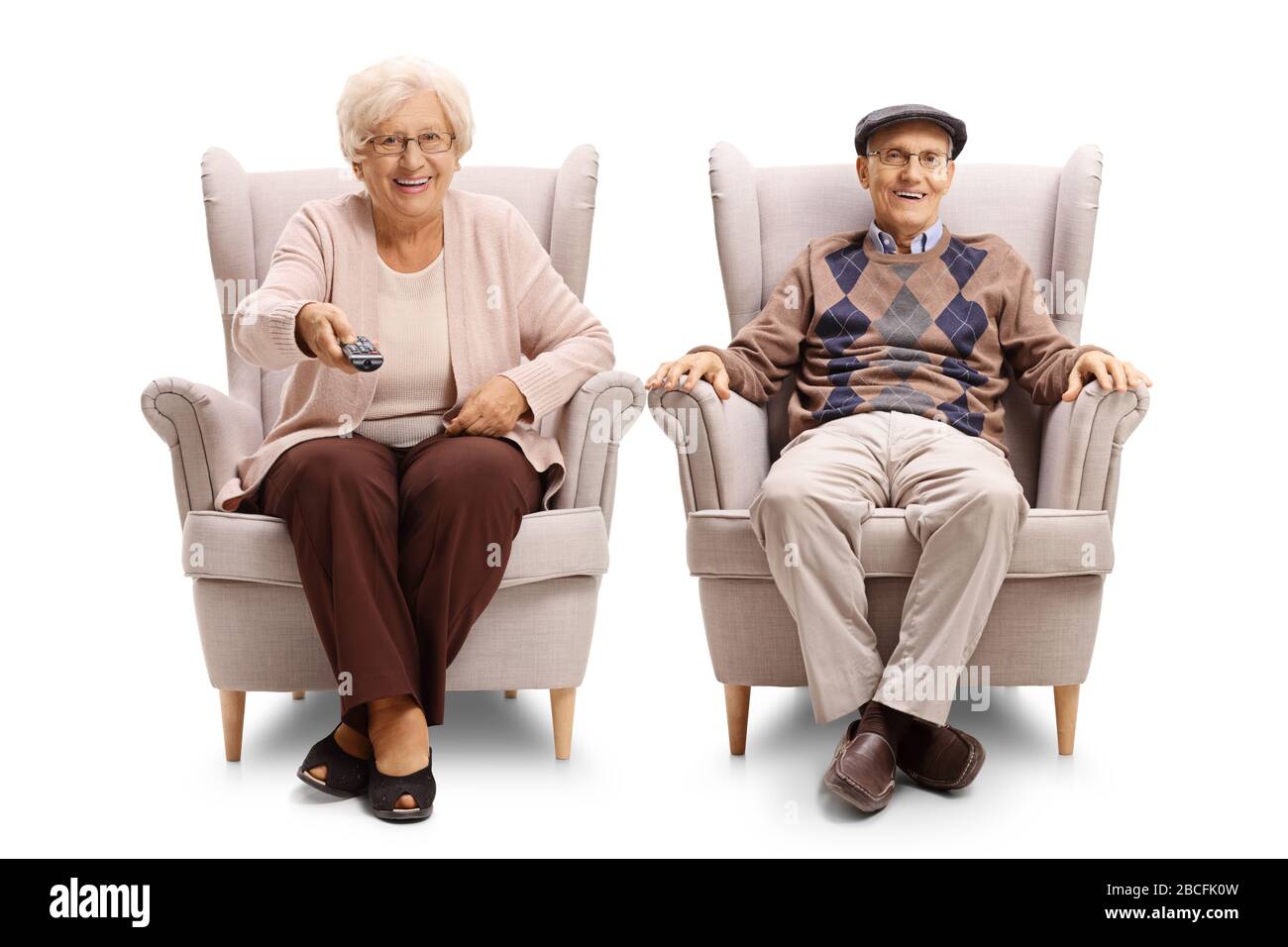 Senior couple sitting in an armchairs and holding a tv remote control isolated on white background Stock Photo