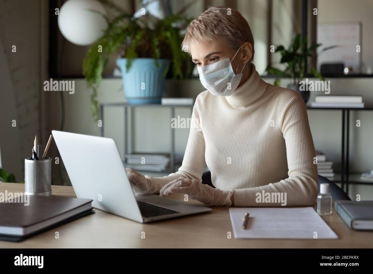 Concentrated young female employee working in medical mask and gloves. Stock Photo