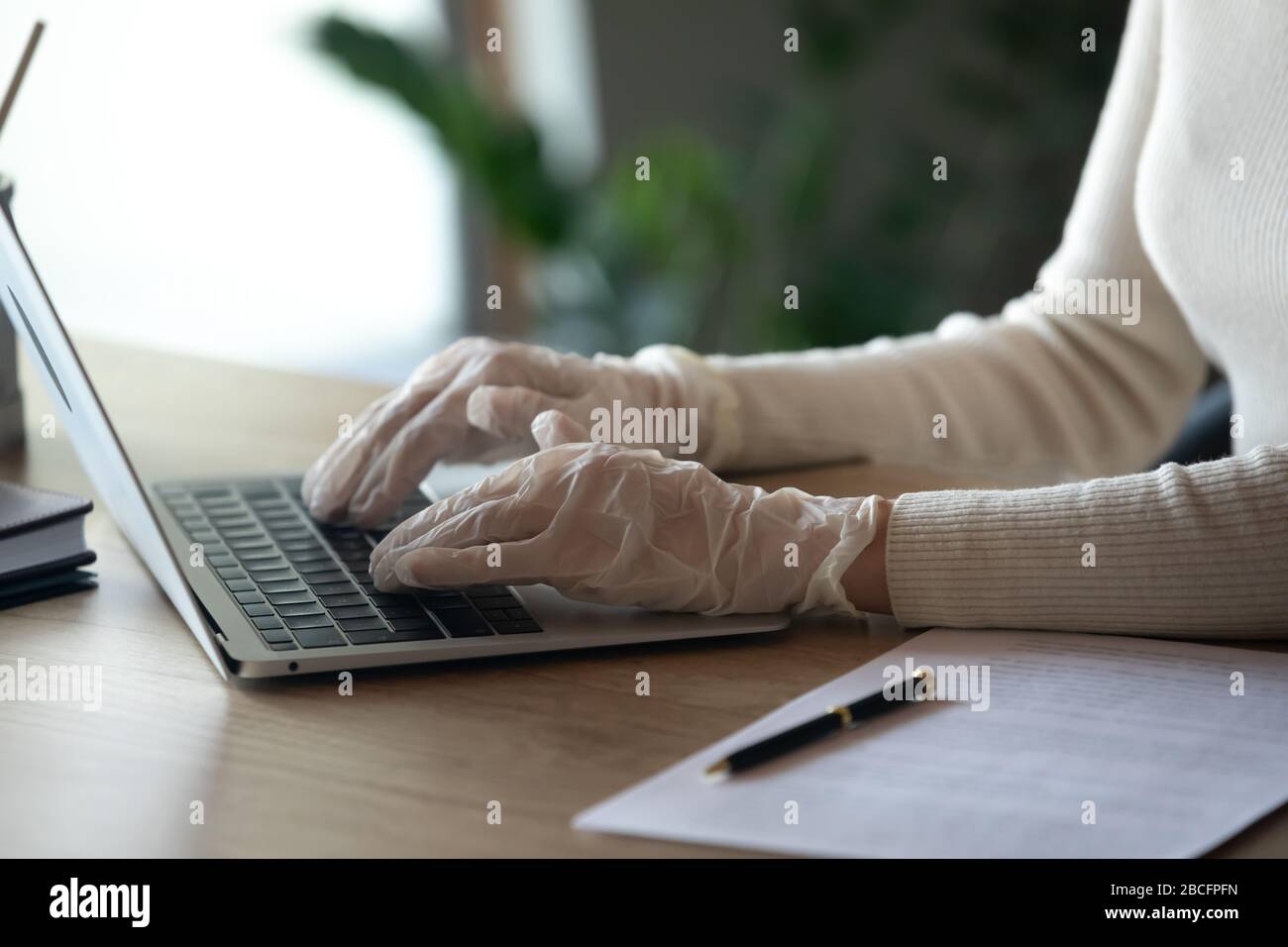 Female hands in protective medical gloves typing on laptop keyboard