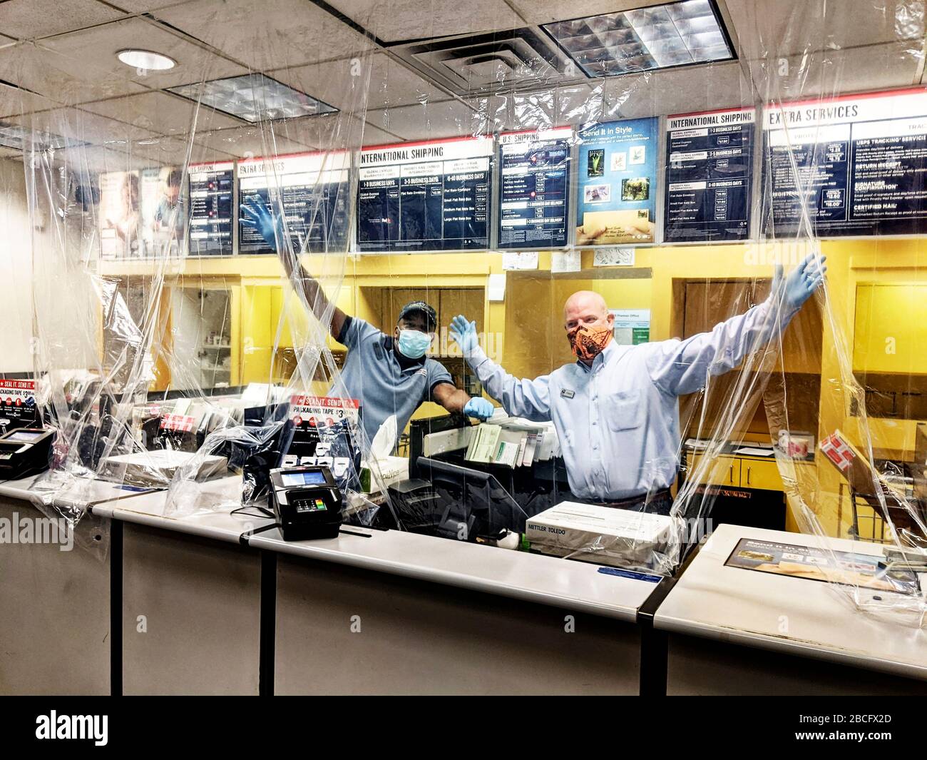 Postal workers wearing gloves and masks deliver the mail rain or  shinealso in pandemic. Post office in Arlington, Texas, with a plastic  sheet hanging from the ceiling between postal employees and customers.
