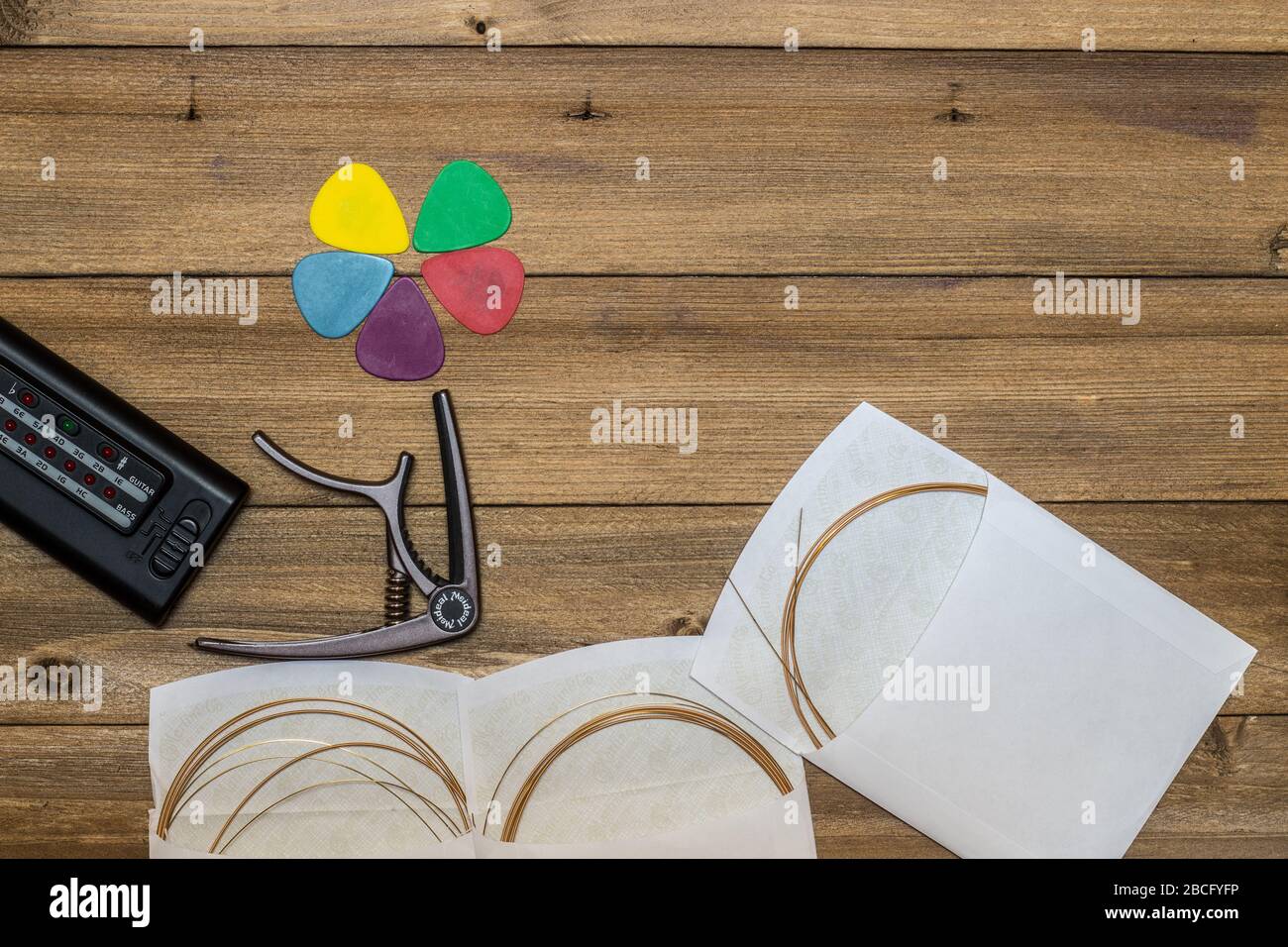 acoustic guitar and its accessories, strings, picks, capo and tuner on wooden background Stock Photo