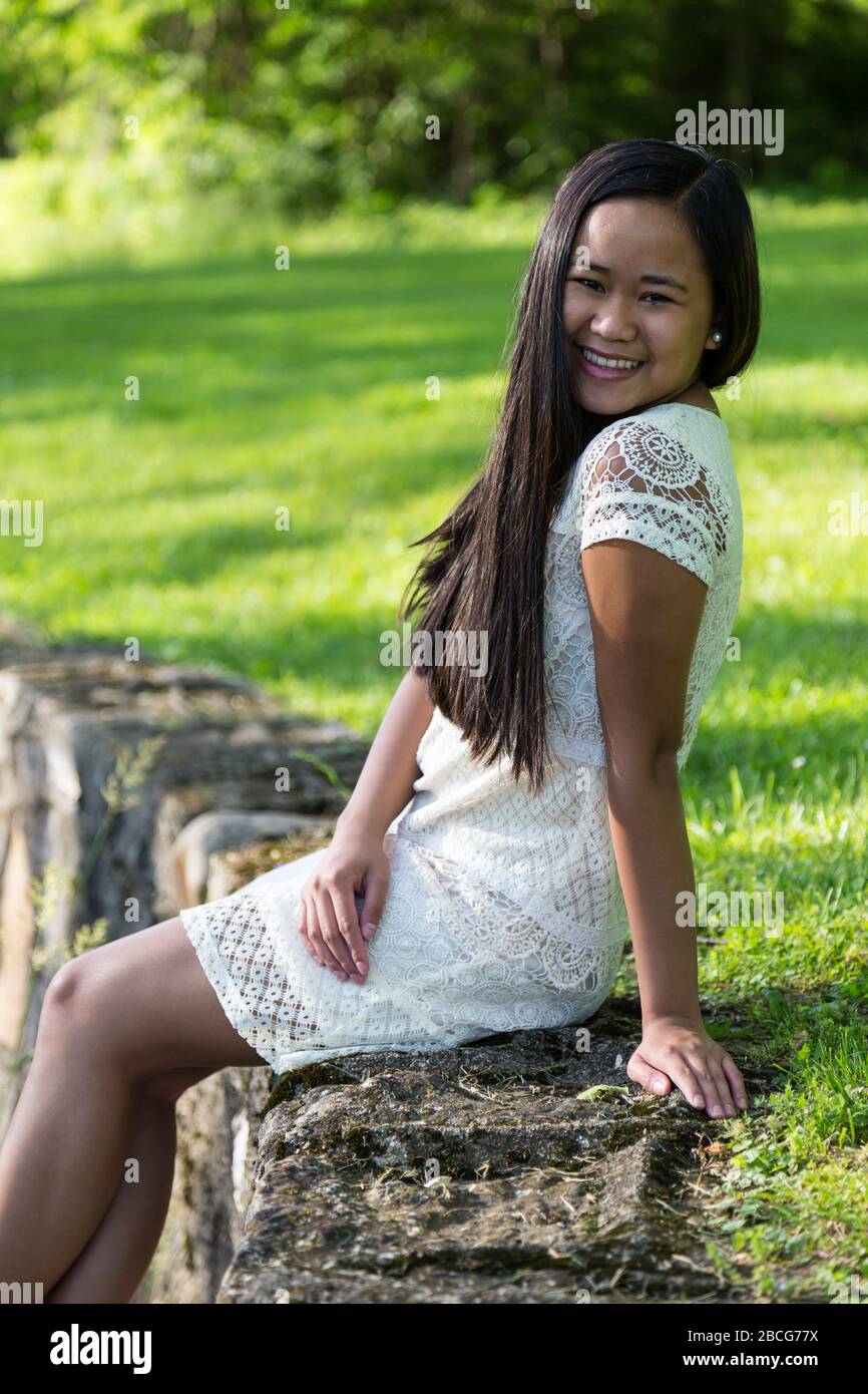 A beautiful young Filipina girl in a white dress poses for her Senior Pictures at Sunken Gardens in Huntington, Indiana, USA. Stock Photo