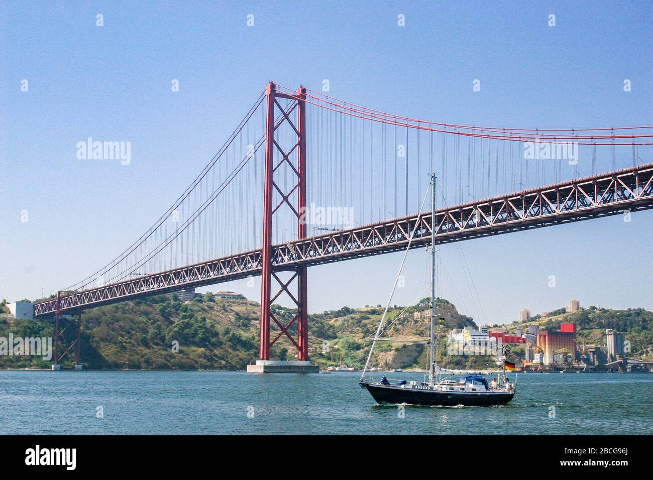 sailing yacht passing the Bridge of the 25 th of April, over the river Tejo in Lisbon, Portugal Stock Photo