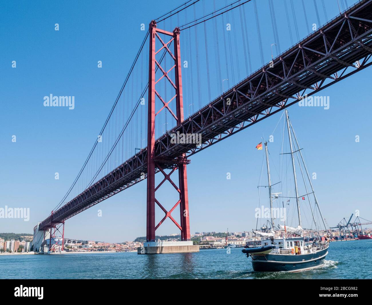 sailing yacht passing the Bridge of the 25 th of April, over the river Tejo in Lisbon, Portugal Stock Photo