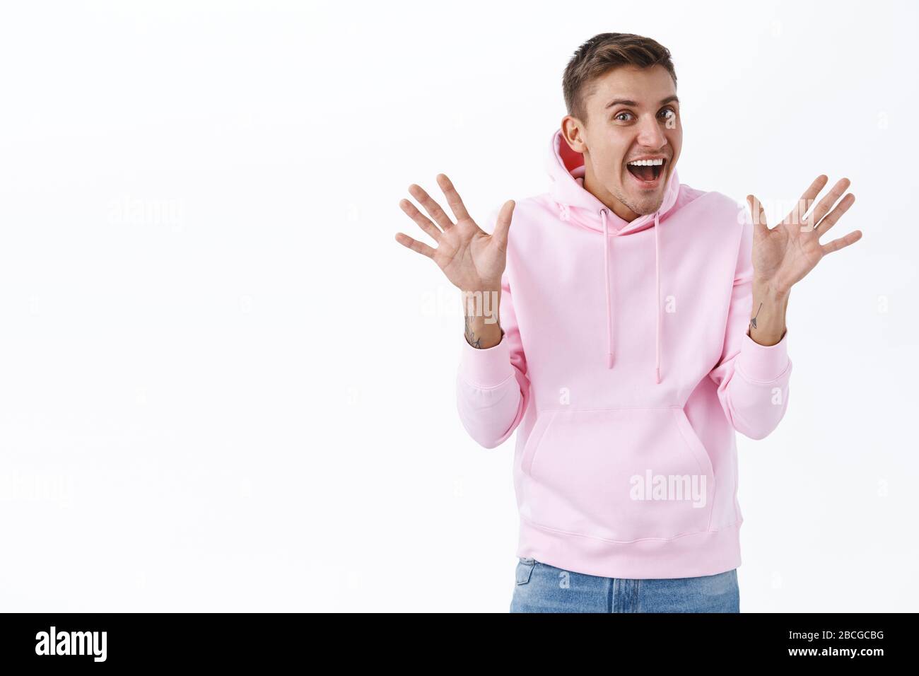 Excited cheerful man with blond hair, make jazz hands, waving palms in hello or hi gesture, saying surprise as congratulating friend with pride month Stock Photo