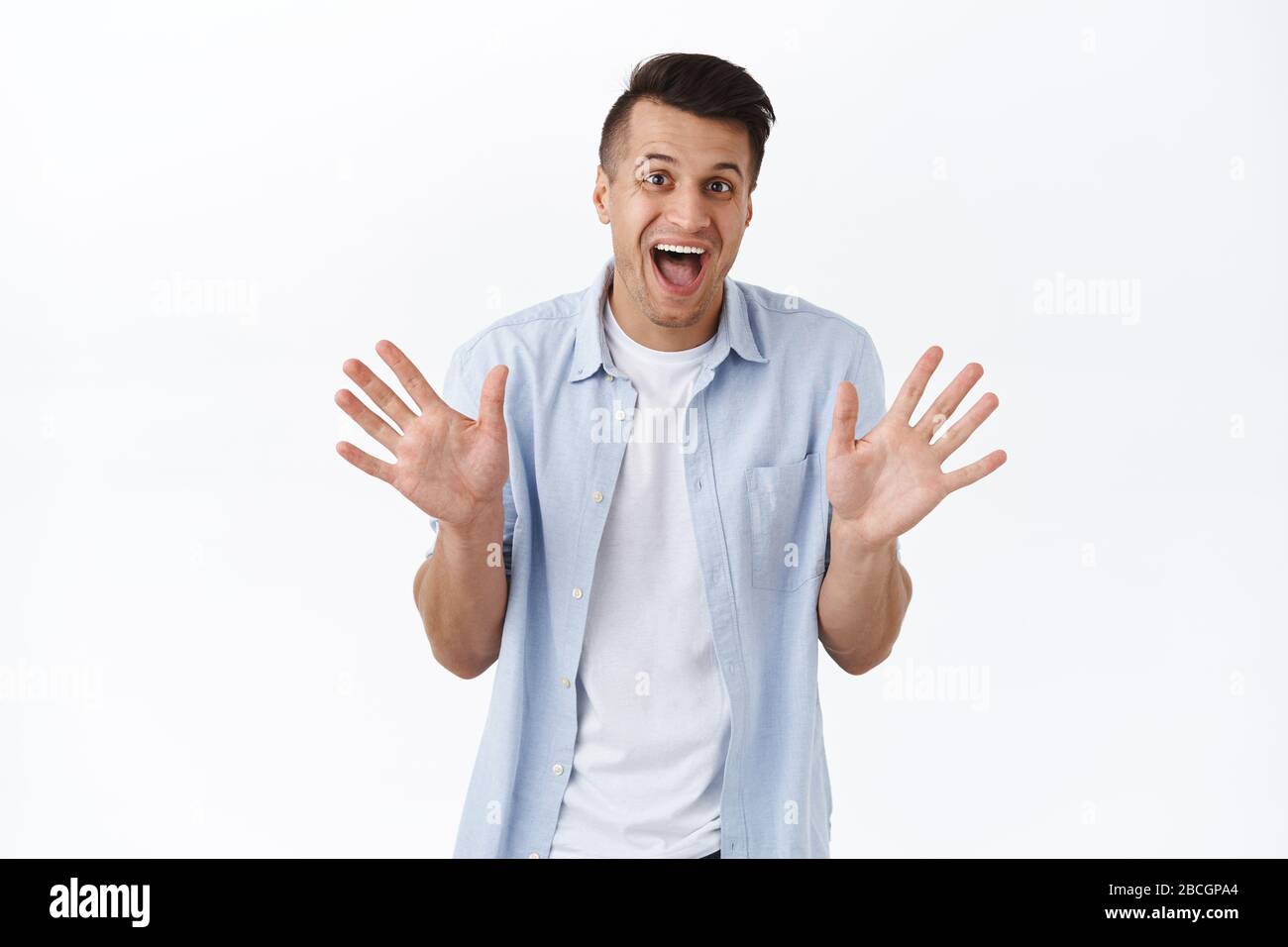 Cheerful handsome happy man make jazz hands, waving empty palms and smiling rejoicing, saying hello or hi to friend, informal greeting concept Stock Photo