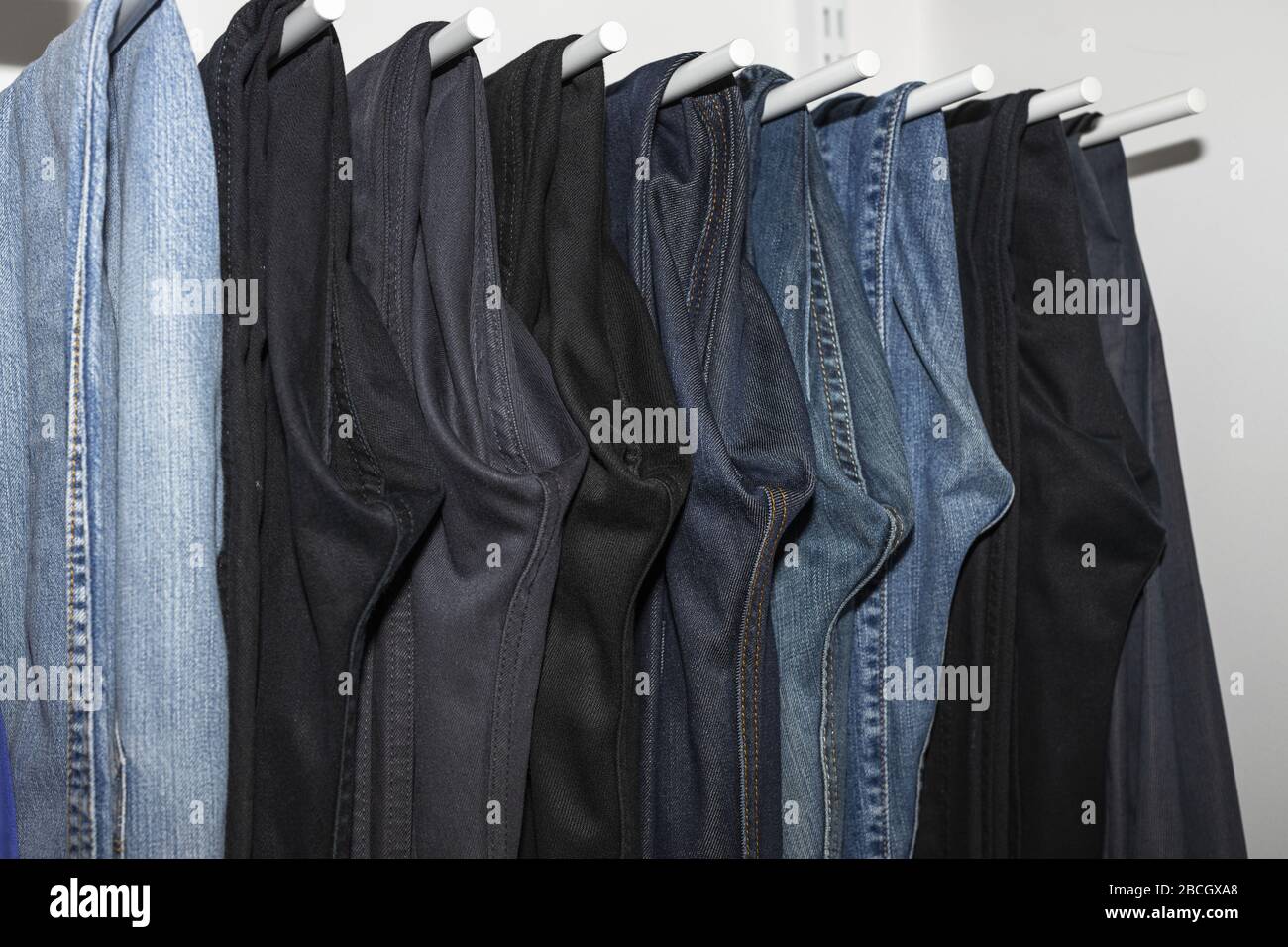 Close up view of interior of built-in wardrobe. Blue and black jeans on white hangers. Cloth organizer. Stock Photo