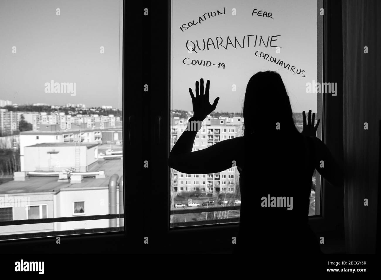 The woman in home quarantine because of the coronavirus. Standing by the window and looking desperately out. Stock Photo