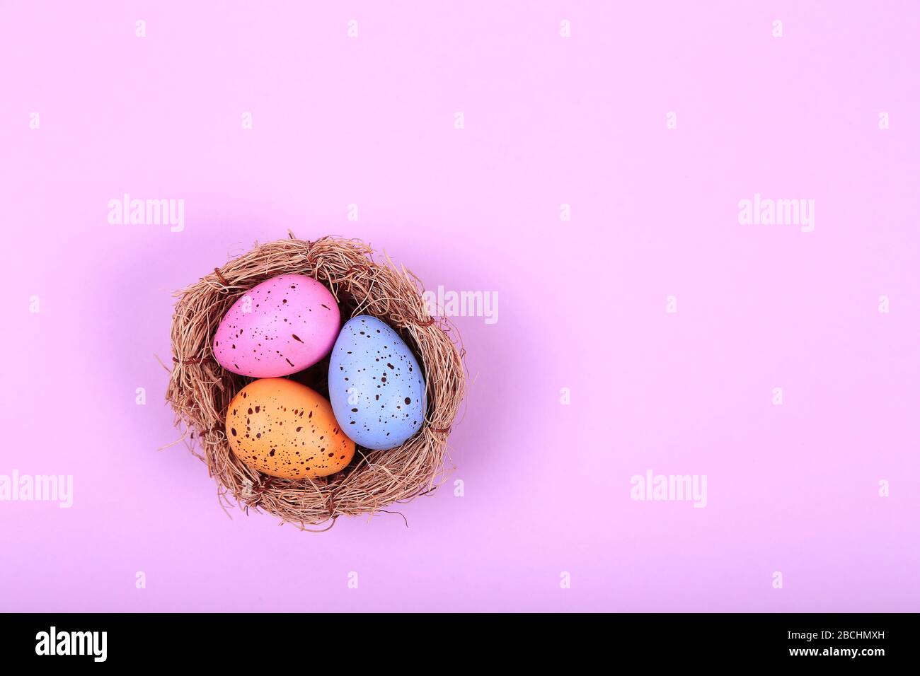 Three colorful easter eggs in nest on pink background Stock Photo