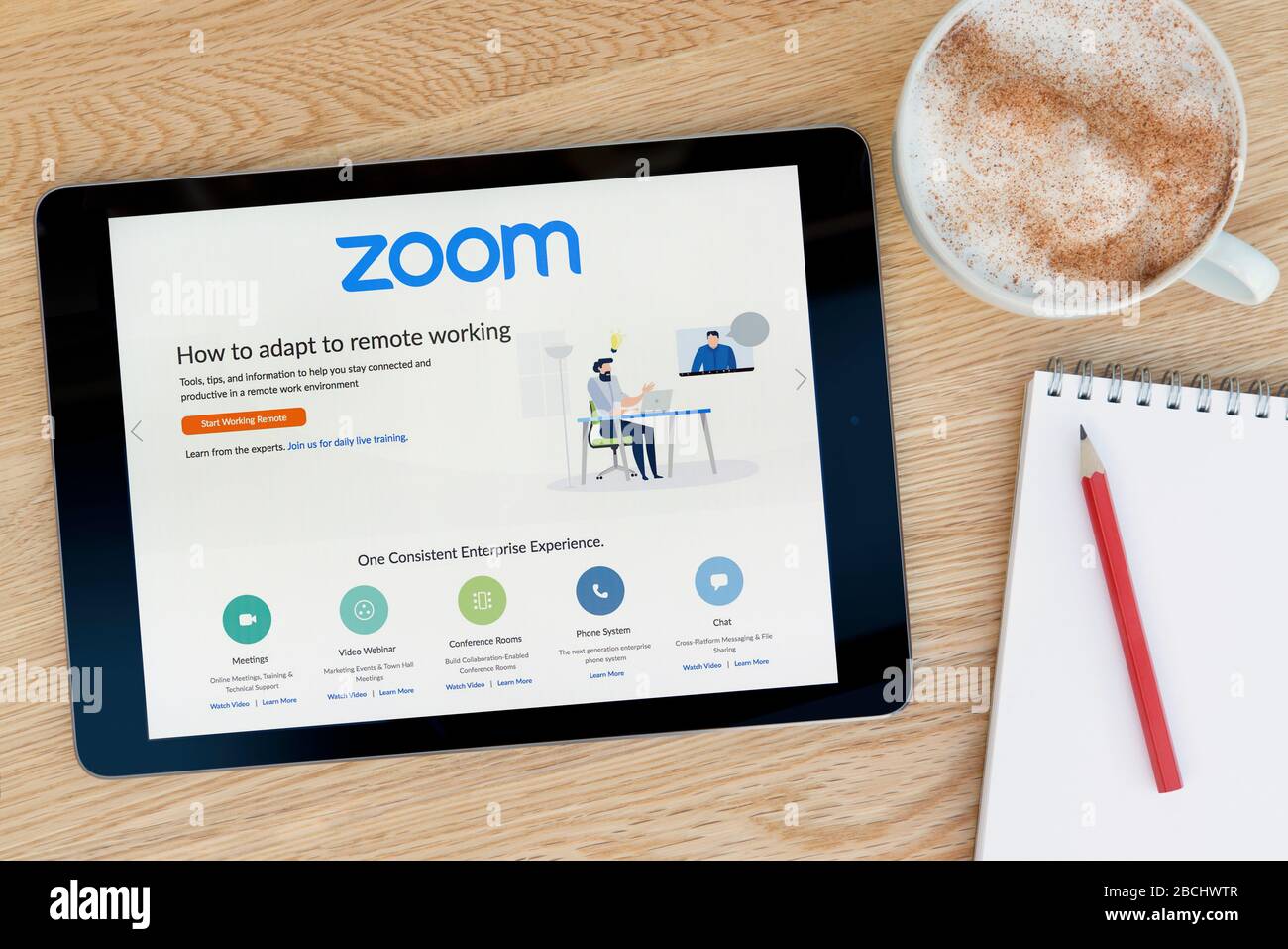 The Zoom video conferencing website features on an iPad tablet device which rests on a wooden table beside a notepad (Editorial use only). Stock Photo