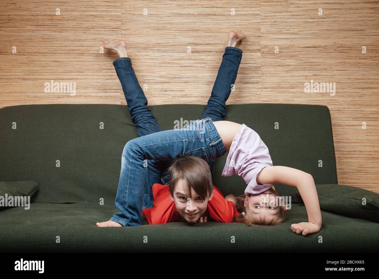 Siblings climbing the walls going mad stuck at home during isolation. Quarantine and lockdown protective measures against spreading of coronavirus pan Stock Photo