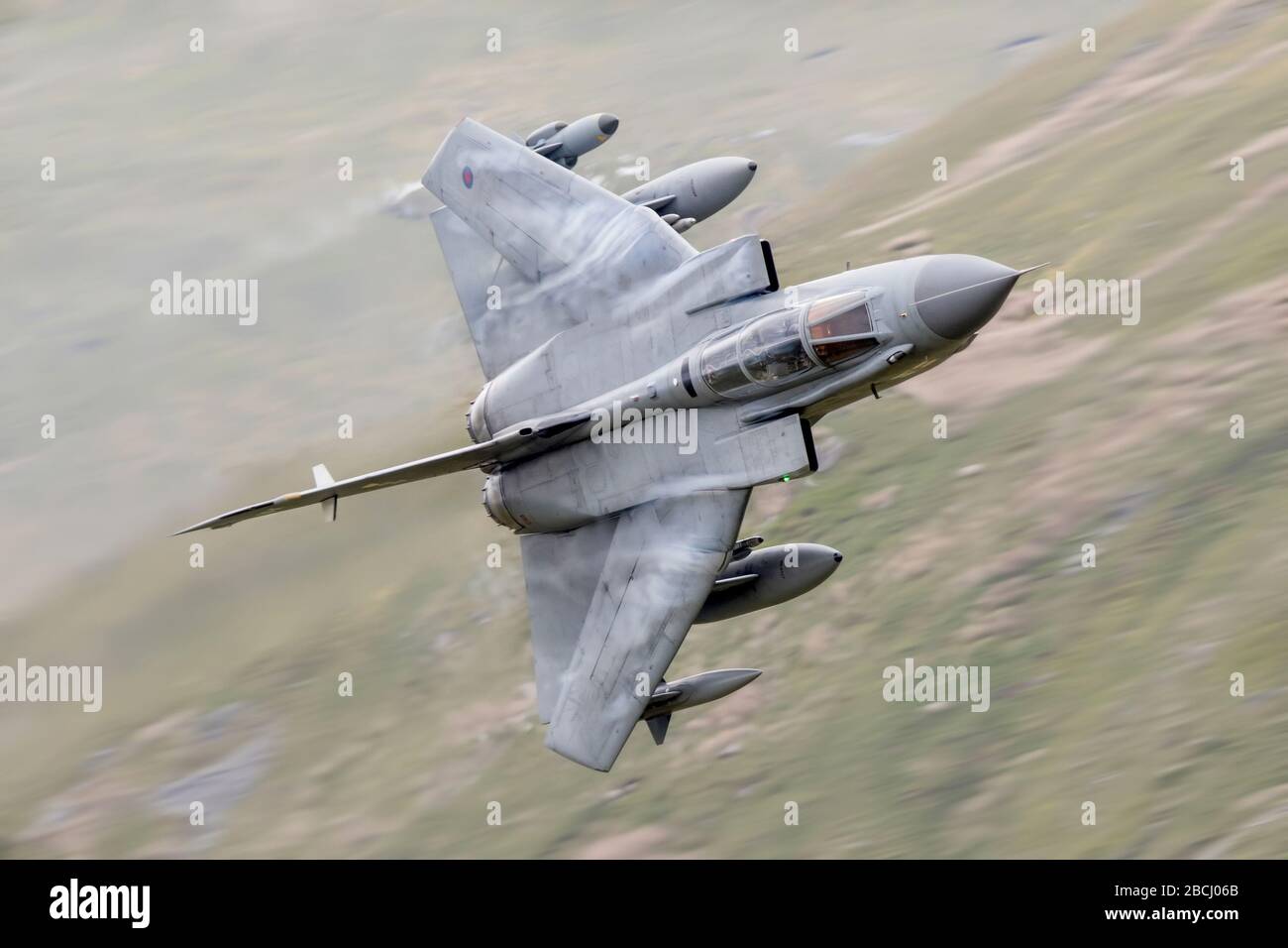 Royal Air Force Tornado GR4 strike attack fighter flying fast and low at low level through a valley with wings sweet back. High speed vapours Stock Photo