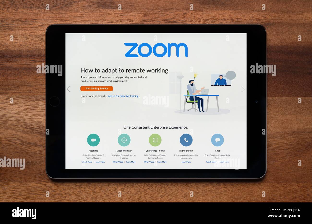 A man looks at the Zoom video conferencing website on his iPad tablet device, shot against a wooden table top background (Editorial use only). Stock Photo