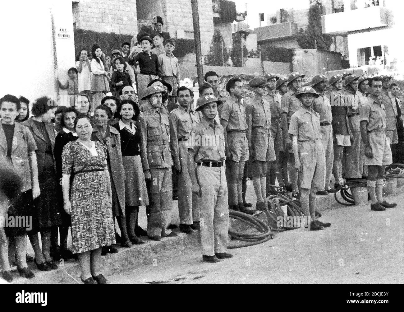 'English: Jewish Civil Defense group in Jerusalem in 1942 (then British Mandatory Palestine). The group served as ARP Fire Wardens, equipped with water hoses and buckets, some wearing FW (Fire Watcher) Brodie helmets. Men are in uniform while women wear plain clothes. Composer Josef Tal stands next to the woman with a black sweater.   Public domainPublic domainfalsefalse      This work or image is now in the public domain because its term of copyright has expired in Israel (details).  According to Israel's copyright statute from 2007 (translation), a work is released to the public domain on 1 Stock Photo