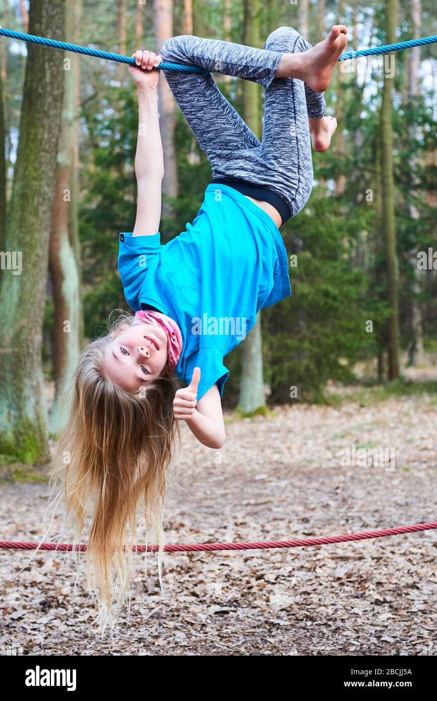 Young child girl hanging on rope upside down on playground in park Stock Photo