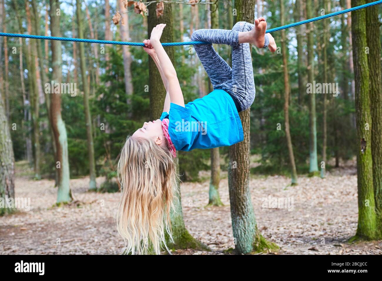 Young child girl hanging on rope upside down on playground in park Stock Photo