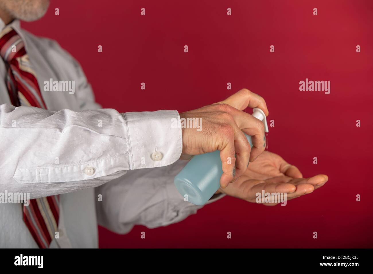 Man using disinfectant gel dispenser for hand washing, against new coronavirus or corona virus disease on a red background. Stock Photo