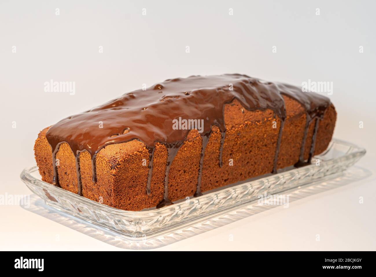a brown cake with chocolate icing stands on a glass plate Stock Photo