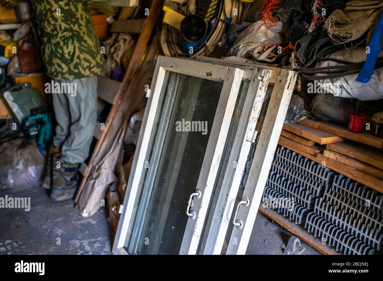 Person man standing inside garage workshop storage room with old glass cold window frames for garden in Ukraine dacha Stock Photo