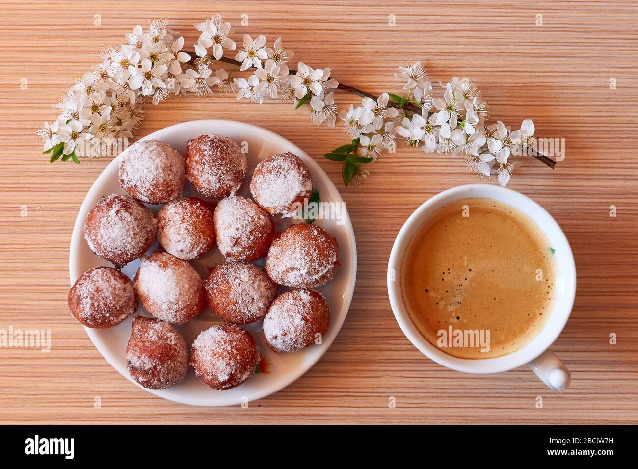 Starting morning with a coffee and homemade donut holes with a blooming brach on desk , during pandemic isolation Stock Photo