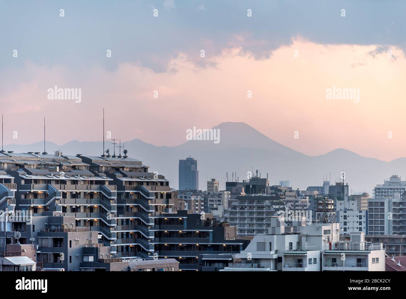 Pink sunset in Tokyo, Japan Shinjuku cityscape with silhouette view of Mount Fuji and golden sunlight, apartment buildings and mountains with rain clo Stock Photo