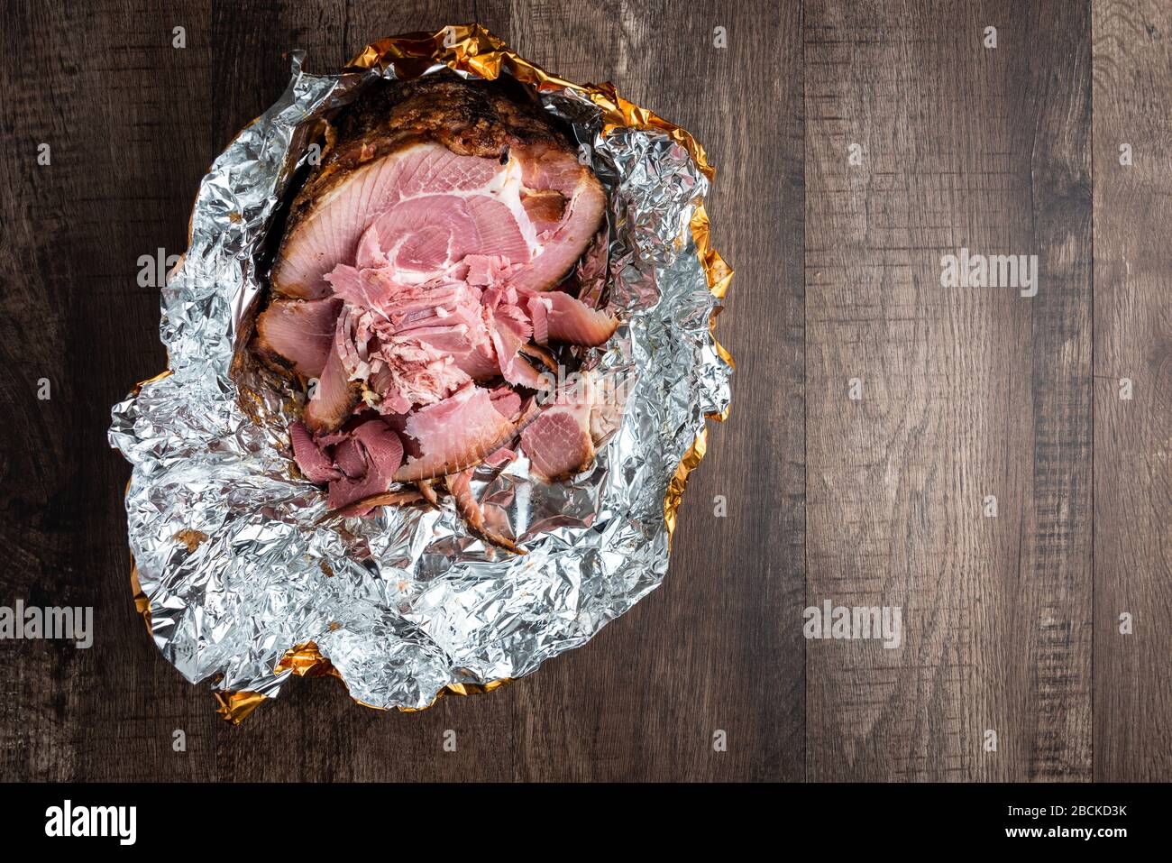 Spiral cut glazed and cooked ham in a foil wrapper on a wood table Stock Photo Alamy