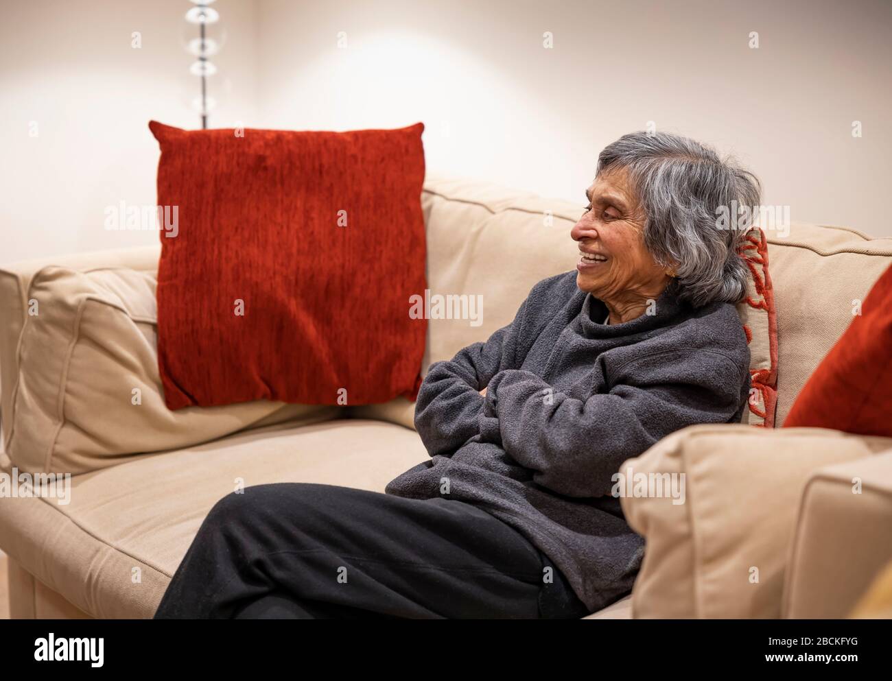 Old elderly, British Asian woman happy watching TV, self isolating during coronavirus outbreak lockdown in UK Stock Photo