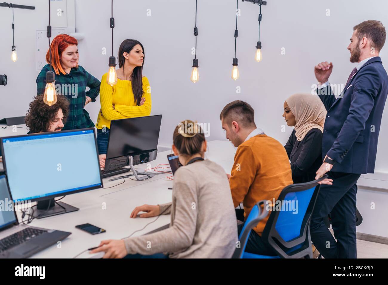 Handsome young executive explaining new employees an online task on theirs computers Stock Photo