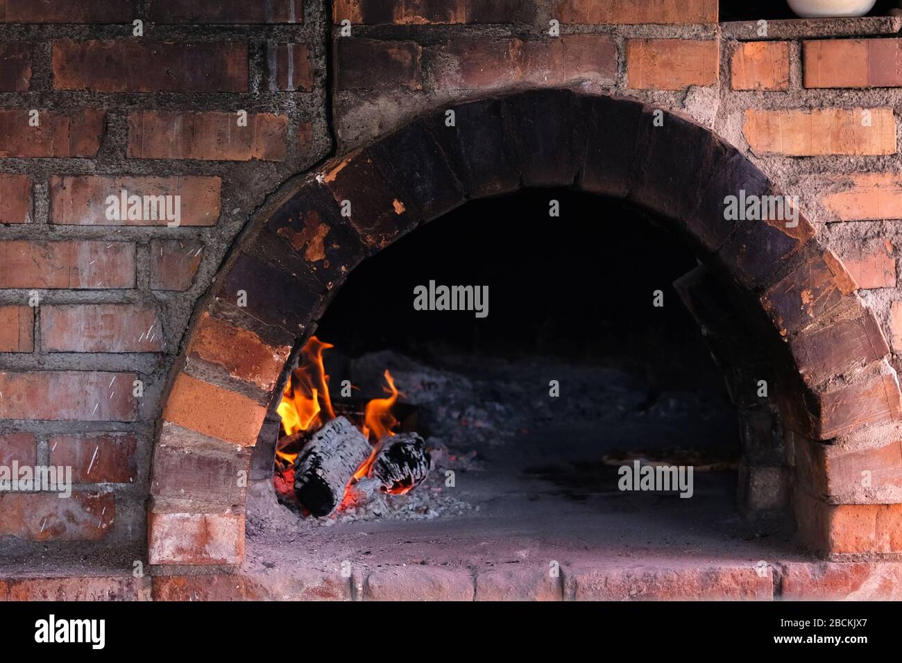 Fire burns in old traditional brick stone furnace for cooking. Cooking in a wood-fired oven. Stock Photo