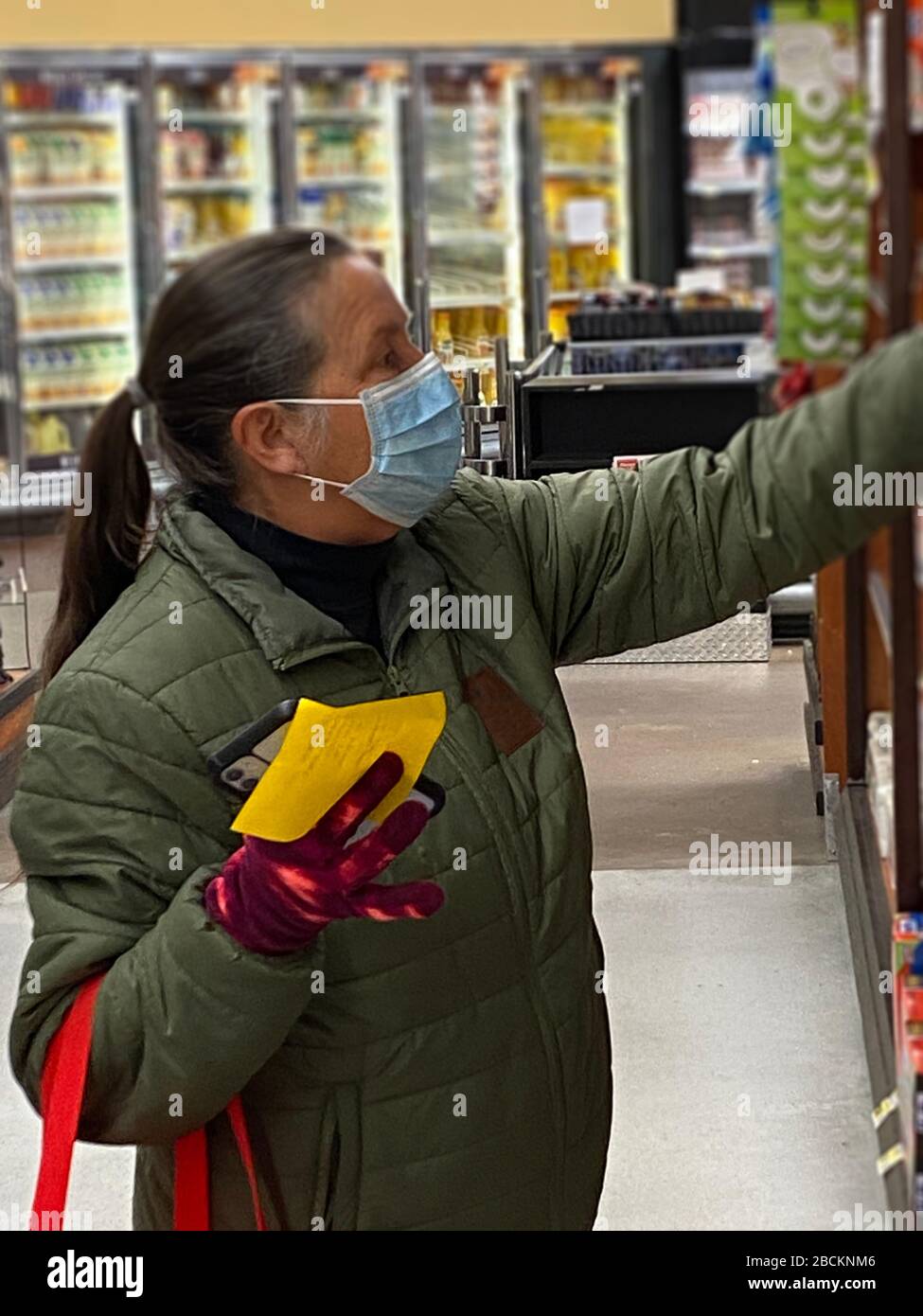 A middle aged woman is food shopping with a surgical mask on during the covid-19 pandemic Stock Photo