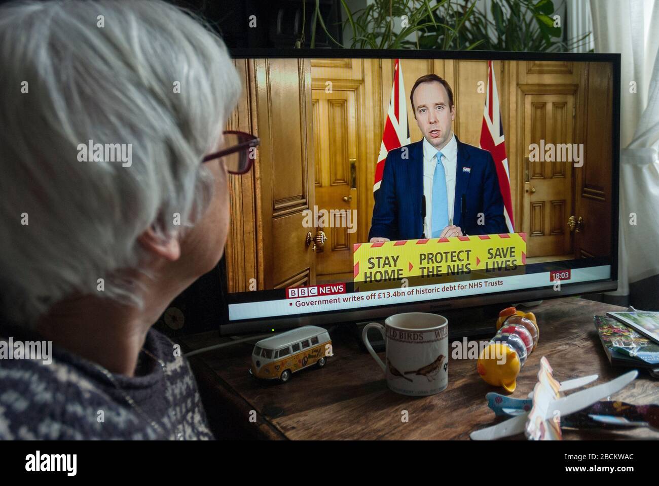 Matt Hancock, Sec of Health, giving a televised broadcast of the daily government Covid-19 briefing. He is watched by an older viewer. Stock Photo