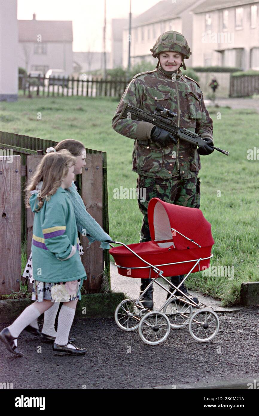 Young Irish girls push a dolls pram past a British soldier patrolling the Bogside area January 25, 1992 in Londonderry, Northern Ireland. Security forces stepped up patrols and searches in the area before the 20th anniversary of the Bloody Sunday massacre. Stock Photo