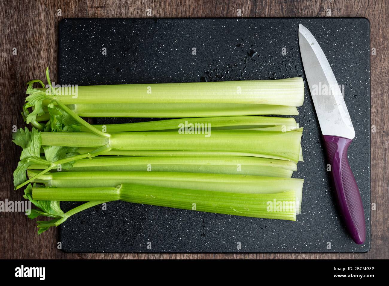Cleaned celery stalks on a black cutting board, chef’s knife, wood
