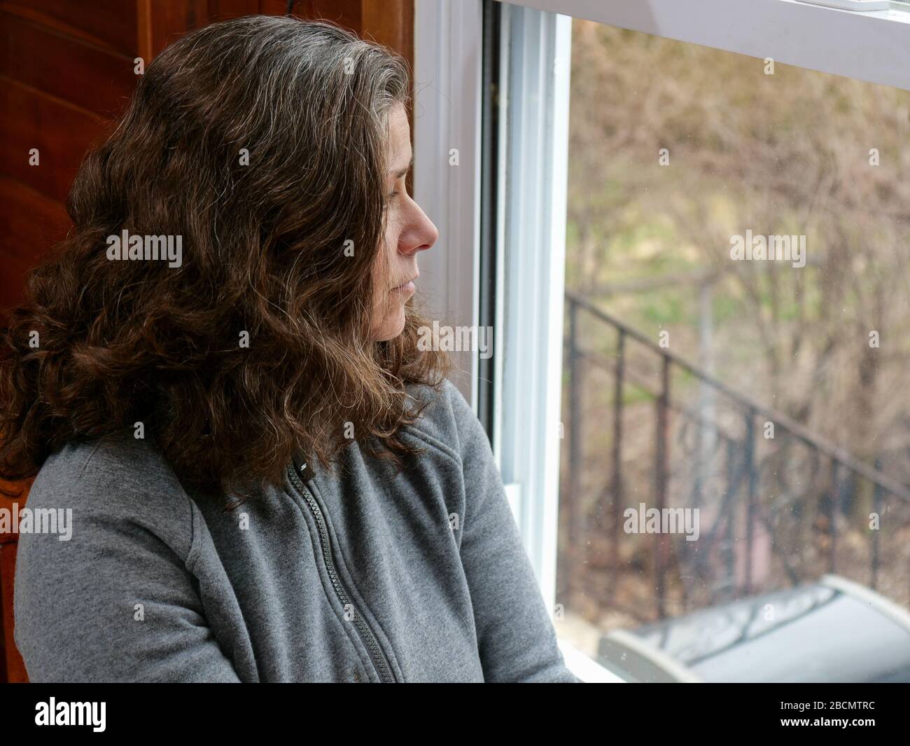 Oak Park, Illinois, USA. 4th April, 2020. A woman looks out her kitchen window during COVID-19 shelter-in-place order. Being stuck at home can bring feelings of isolation and loneliness. Stock Photo