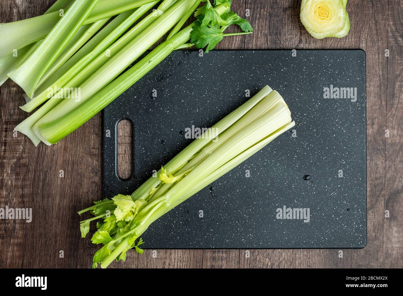 Celery stalks washed and ready to chop on a black cutting board, wood table Stock Photo
