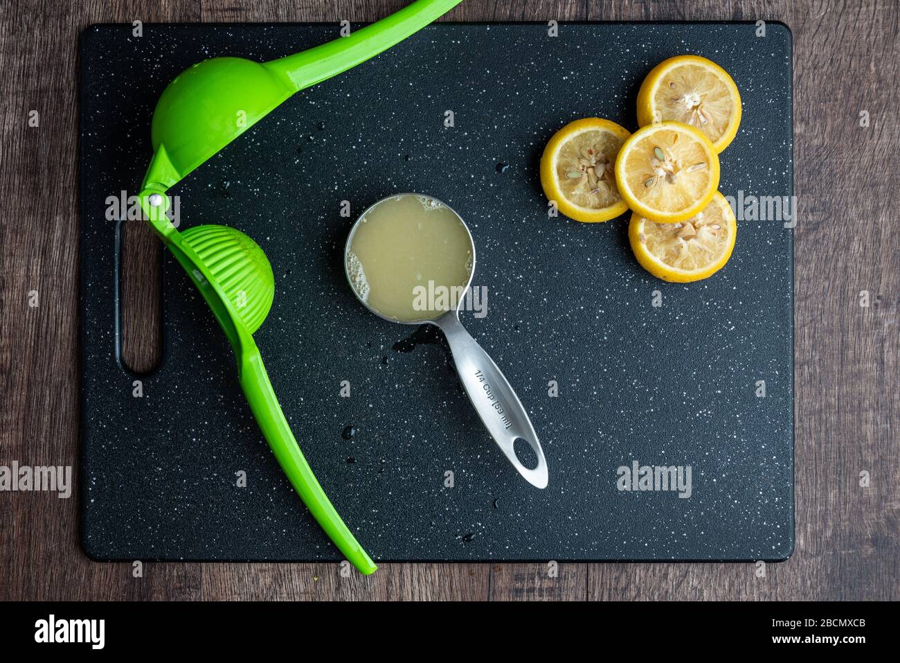 Fresh squeezed lemon juice in measuring cup, citrus squeezer, lemons