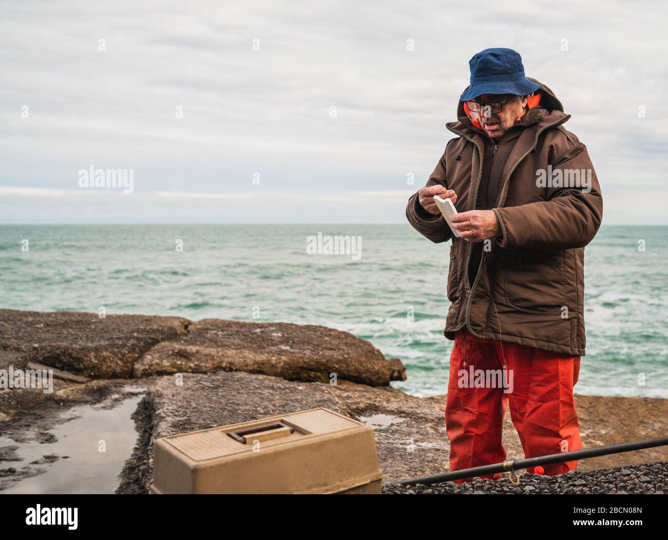 Portrait of a fisherman putting on bait with fishing equipment box. Fishing and sport concept. Stock Photo