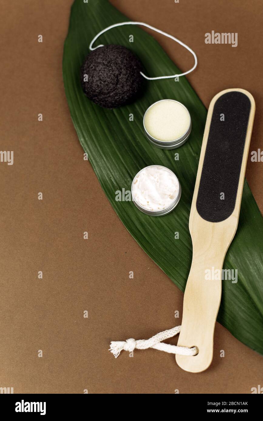 Palm leaf with natural various pumice for exfoliating the skin lie on a brown background with copy space. The concept of moisturizing the skin of the feet with a cream, lotion or balm. Stock Photo