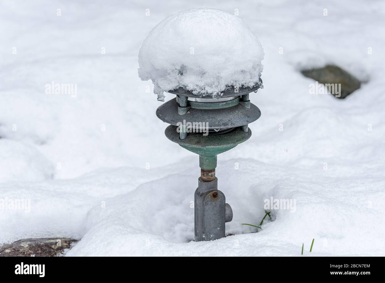 Fresh wet snow covering a garden, old metal light fixture poking out Stock Photo