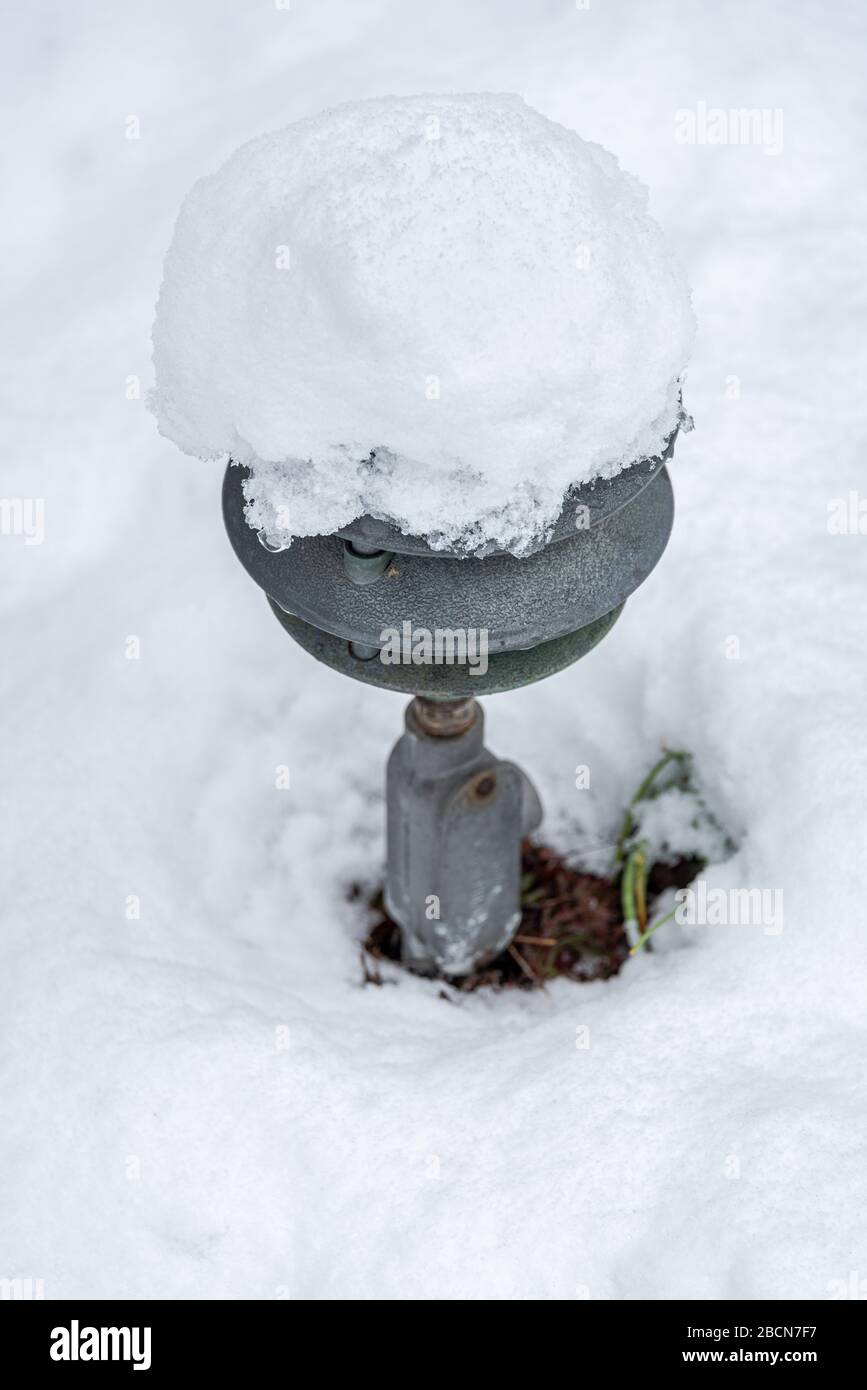 Fresh wet snow covering a garden, old metal light fixture poking out Stock Photo
