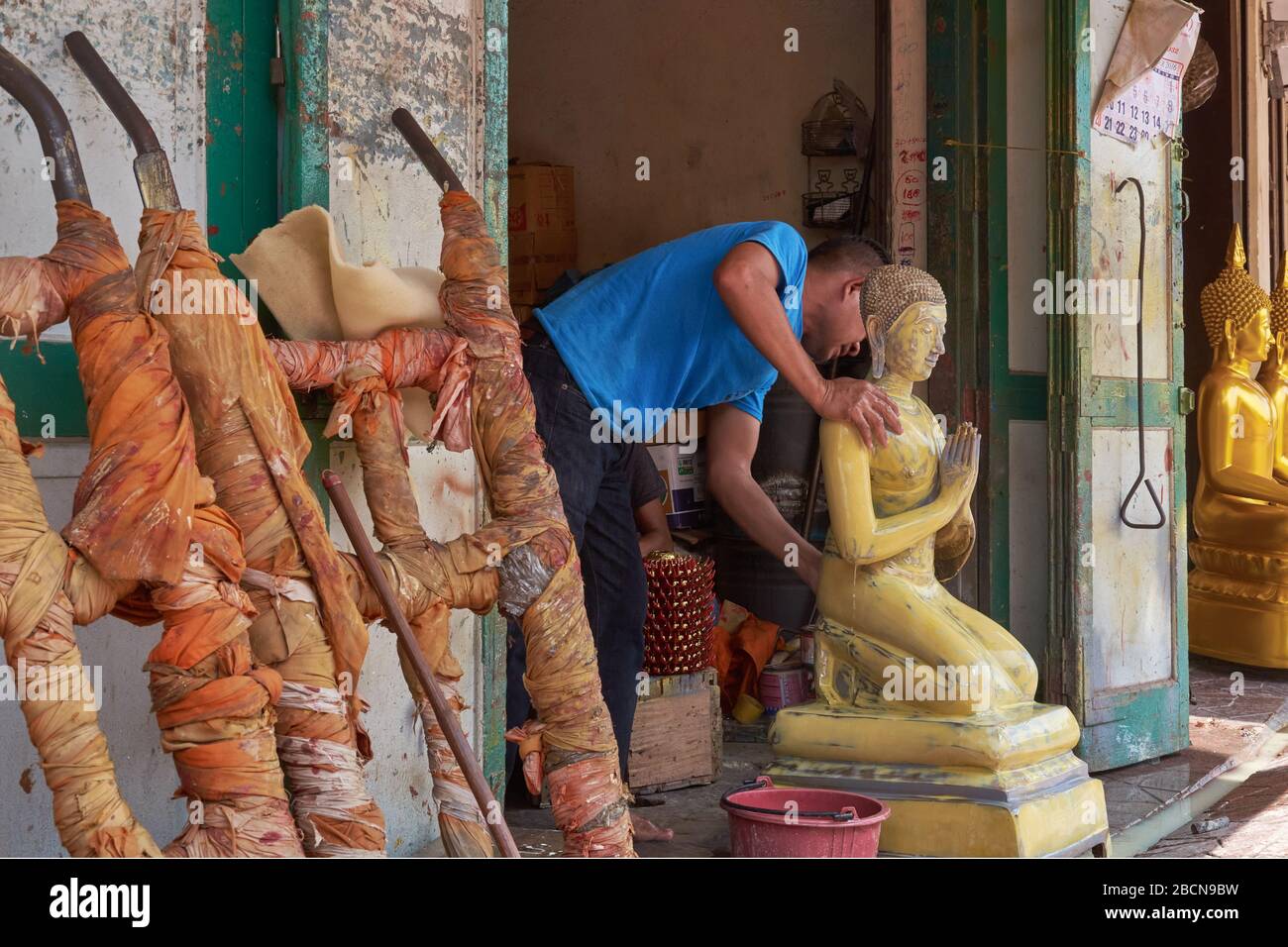 An employee in a factory for Buddha statues in Bamrung Muang Road, Bangkok, Thailand, moves an unfinished statue of a kneeling and praying Buddha Stock Photo