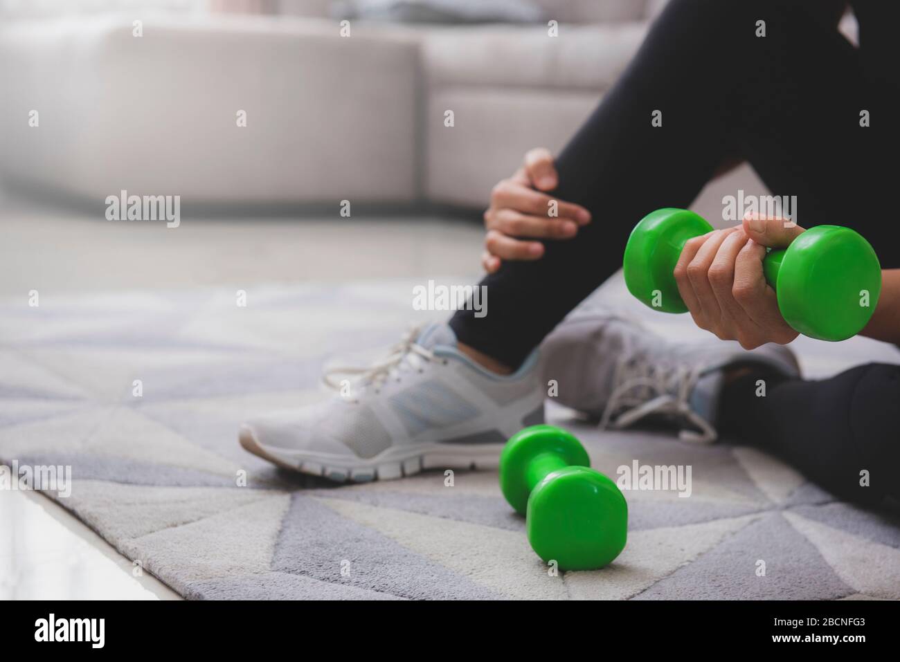 A sporty woman in sportswear is sitting on the floor with dumbbells. Sport and recreation concept. stay at home campaign for coronavirus prevention. Stock Photo