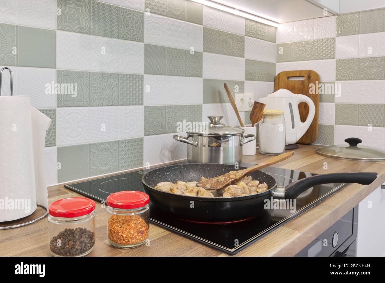 The meat is fried in pan on hob. Kitchen interior, cooking utensils
